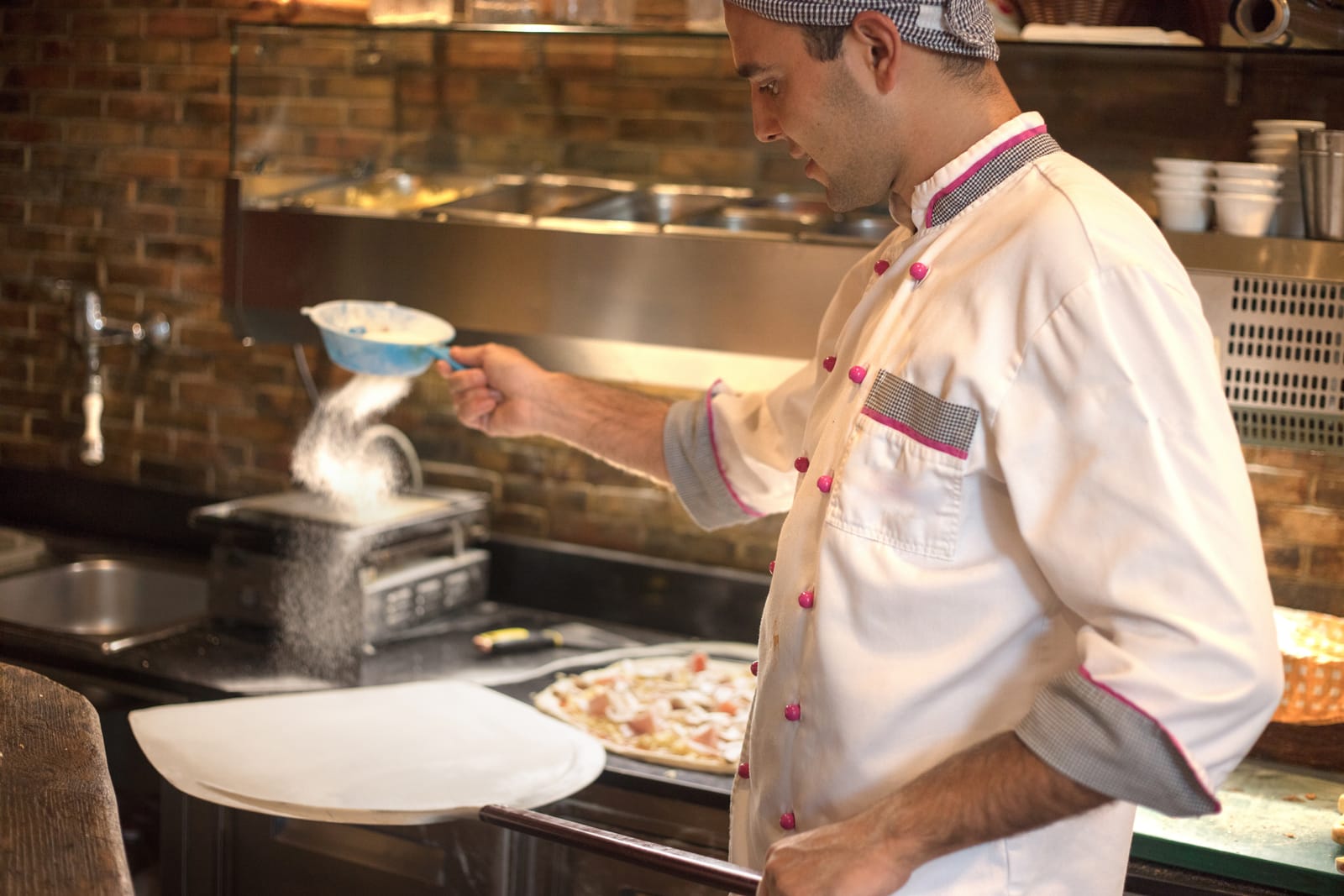 A restaurant chef sprinkles flour on pizza dough on pizza paddle
