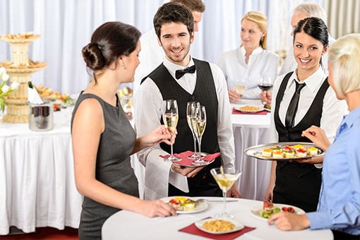 Guest taking champagne from waiter's tray and waitress offering another guest hor d'oeuvres